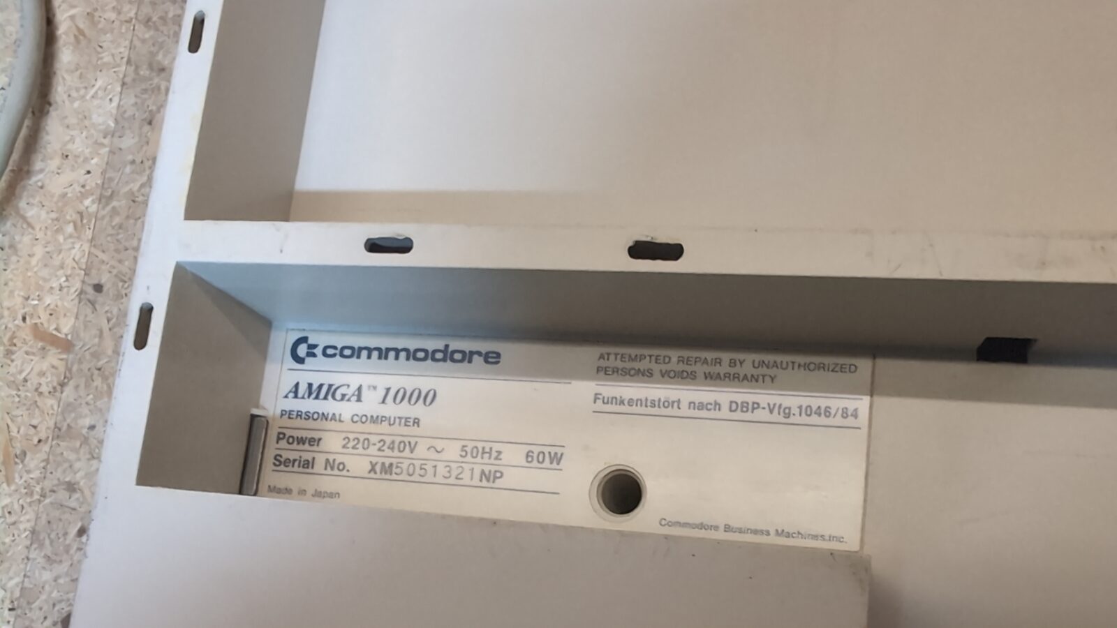 Close up of the inside label of a Commodore Amiga computer, showing model information, serial number, and power requirements on a white background retrohax net