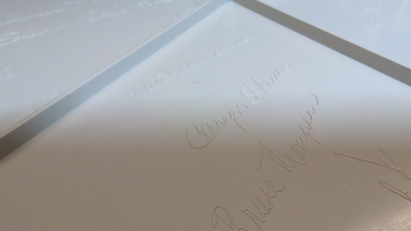 A close up of white glossy surfaces with several faint, engraved signatures written in cursive, partially illuminated by soft light The signatures are subtle and blend with the shiny background retrohax net