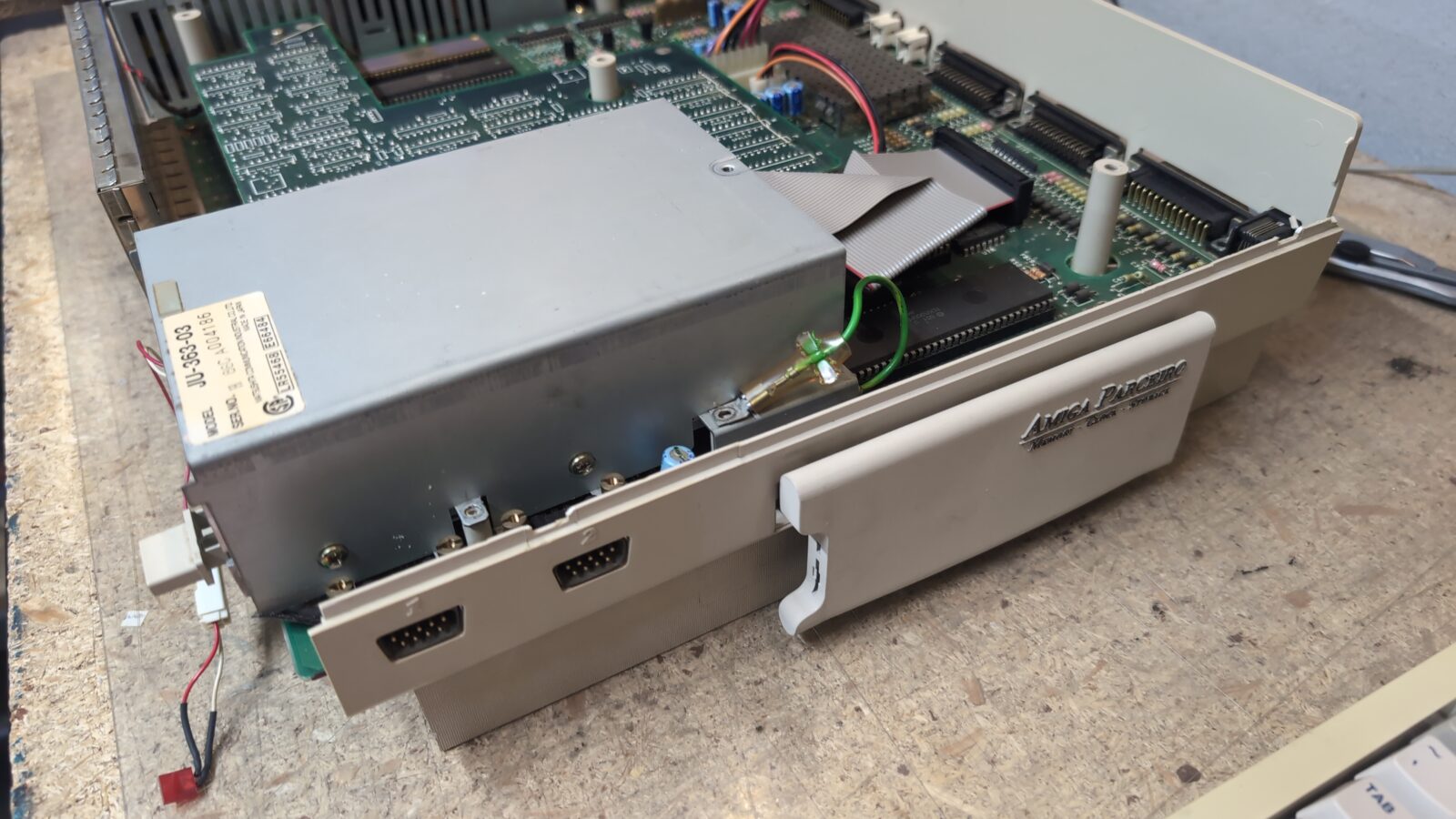 Open vintage computer case showing internal circuit board, connected cables, and a large metal shield The case front displays Amiga , two controller ports, and a removable expansion slot cover on a textured surface retrohax net