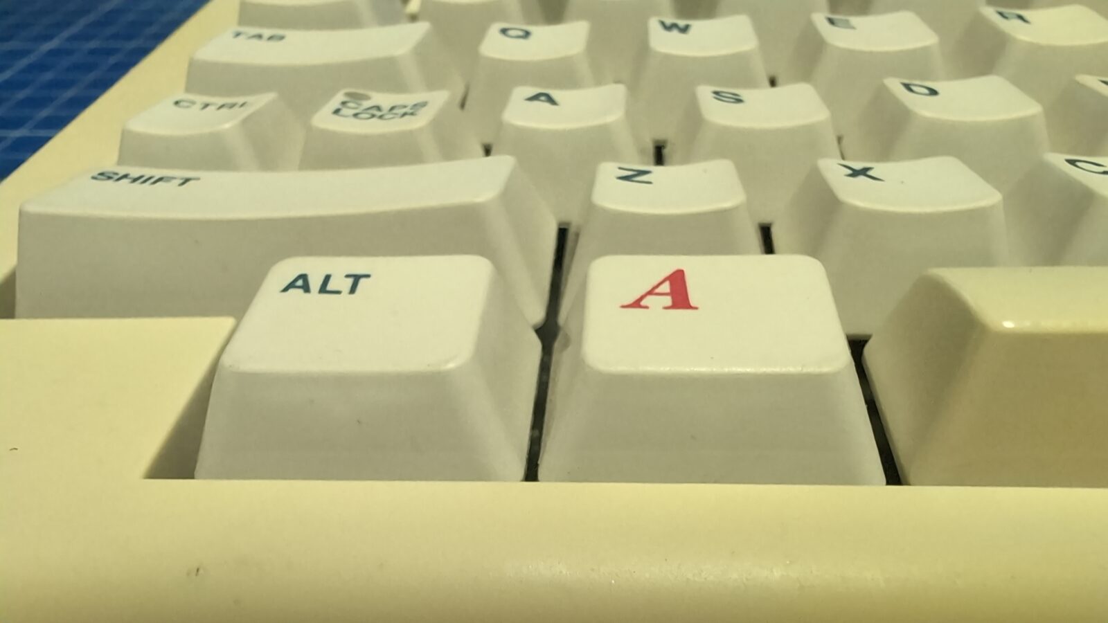 Close up of a vintage computer keyboard, focusing on the ALT and A keys, with other white keys and part of the beige keyboard frame visible in the background retrohax net